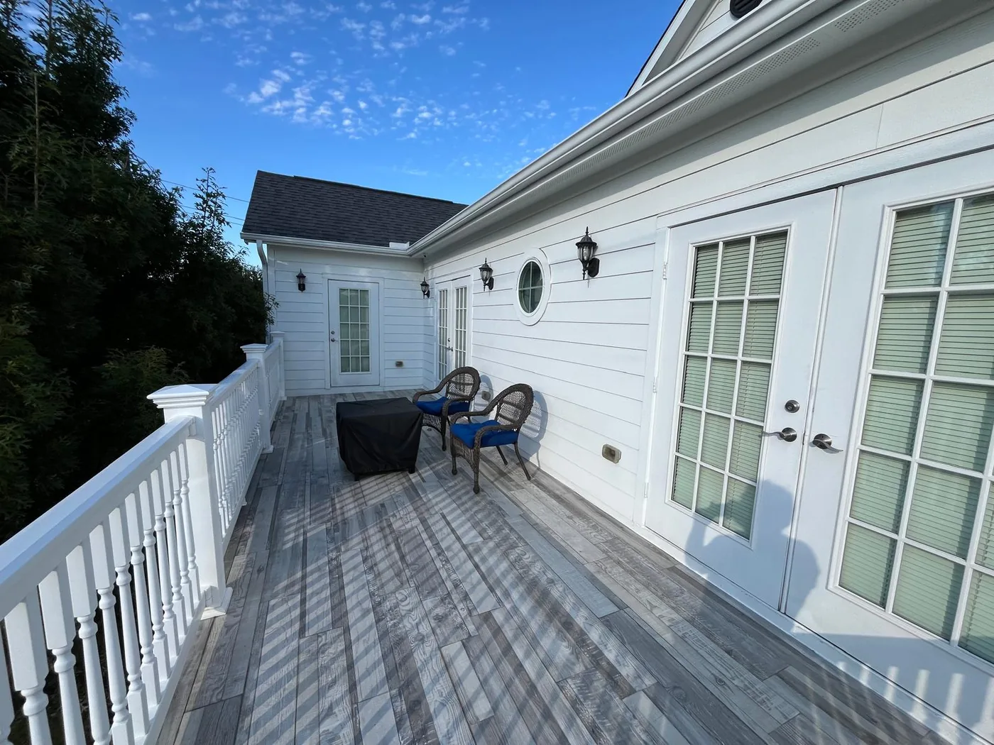 The upstairs balcony with white railings, two wicker chairs and french doors from the guest rooms