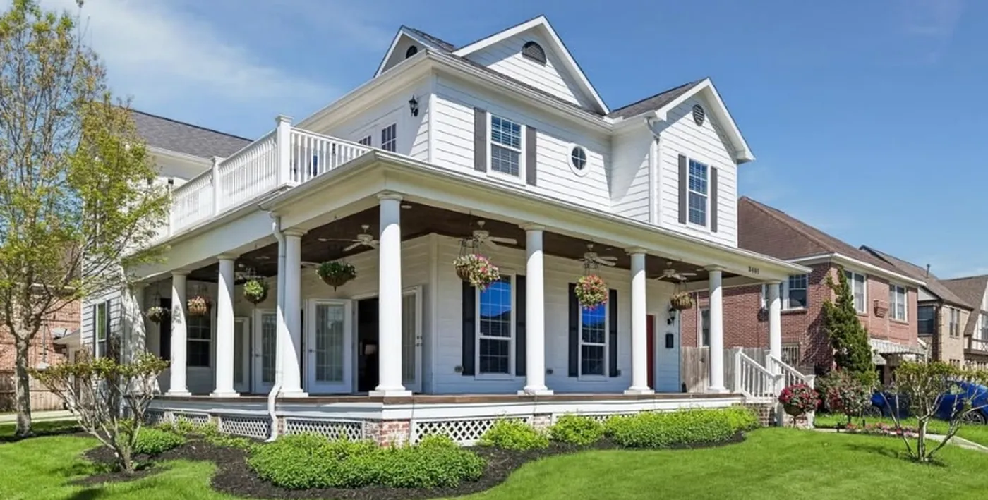 The guest home, a white two story house with a deep wraparound porch, white columns, a second floor balcony and a red front door, set behind a wide green lawn